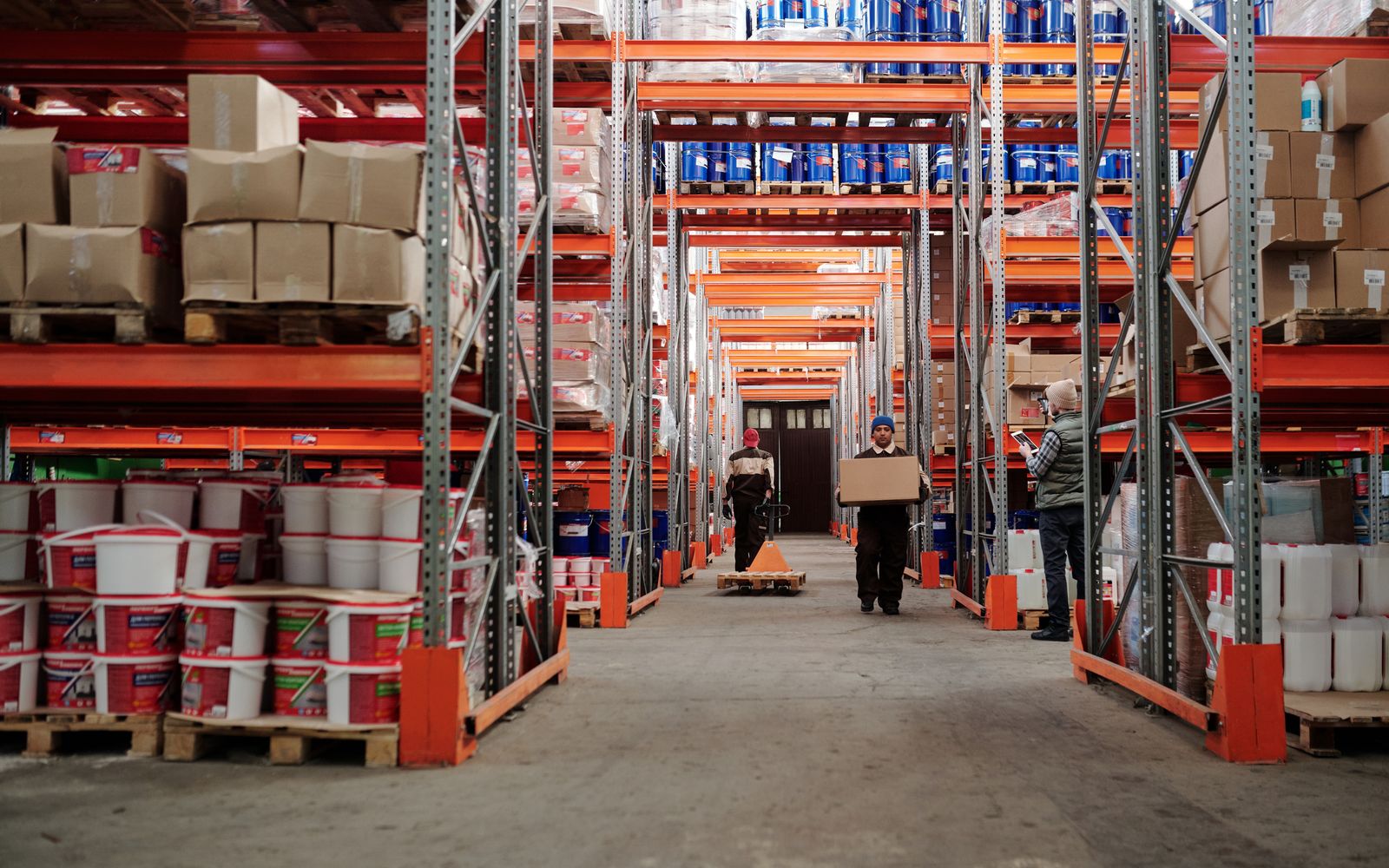 Warehouse workers moving cardboard boxes among stocked racks
