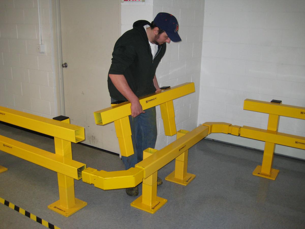 Worker installing yellow steel guardrails inside an industrial workplace