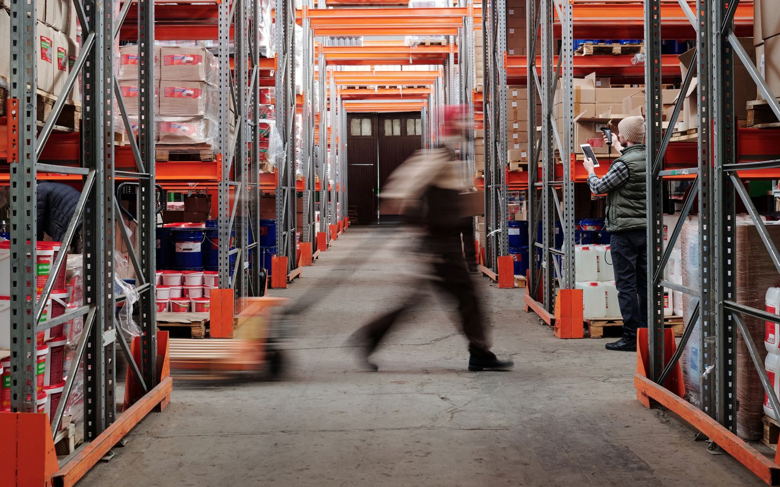 Workers in an aisle of tall warehouse pallet racks